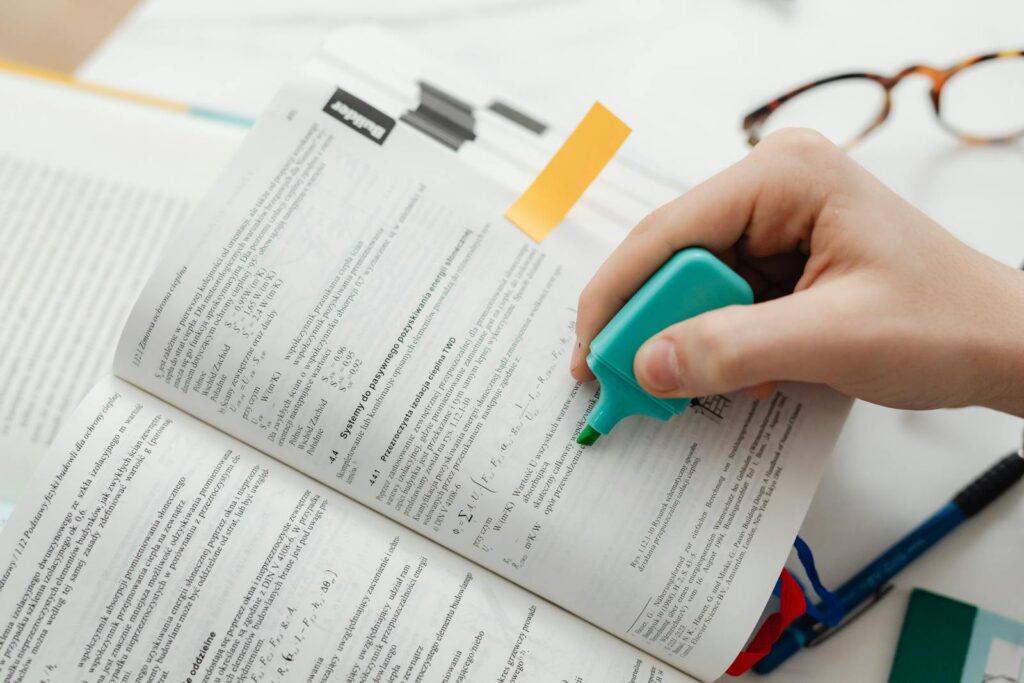 Close-up of a hand using a highlighter on an open textbook, focusing on key information.